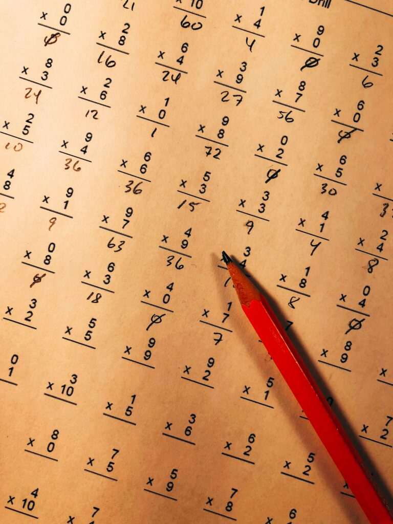 A red pencil resting on a maths worksheet